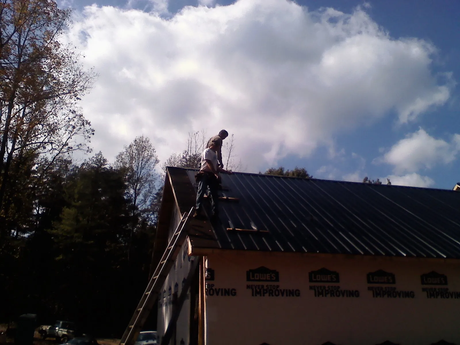 Roofer fastening dark metal panels high against a cloudy sky, from a Roof Inspection job in Millington